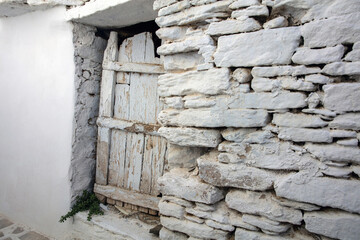 Aged white stonewall background, door covered with broken peeled plank. Cyclades island, Greece.