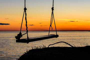 Empty swing hanging from the tree at bank of river Dnieper at sunset