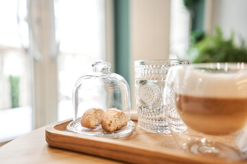 Cup of coffee cappuccino with cantuccini and a glass of water on a wooden tray. Coffee with milk, a cookie and a glass with water on a glass table.