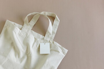 Eco bag for shopping with blank tag on beige background top view , copy space.