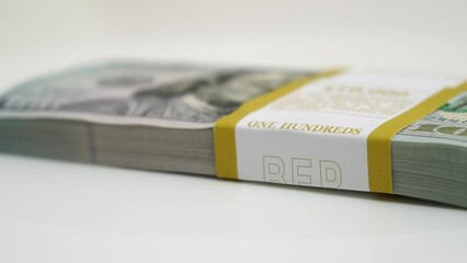 stack of bank bundles with US dollars on a white background. Close-up shot of new, freshly printed hundred-dollar bills rotating on a table. cash flow, business investment, or big money concepts. - Powered by Adobe