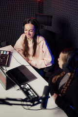 View from above. Female host and guest sitting at table with equipment while broadcasting radio program in recording studio. Women speaking during radio program in studio