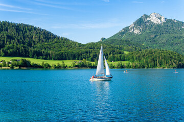Sailing boat in the lake against the background of mountains and green forest. Sailboat floating on...
