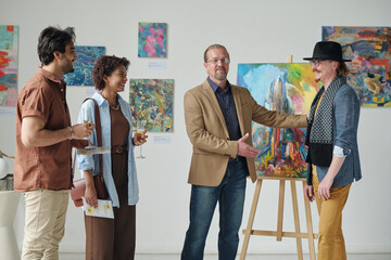 Gallery owner presenting artist of art gallery to group of people during exhibition