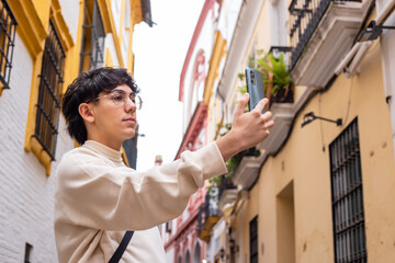 Obraz na płótnie Canvas twenty-year-old boy with glasses and brown hair, takes a picture with his cell phone of the streets of the center of Seville, Spain