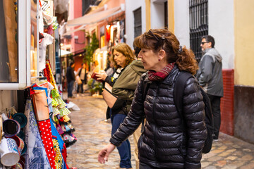 Fototapeta na wymiar Fifty-year-old woman walks with her family through the native shops of Seville, Spain. She is looking at some cups and flamenco-style dresses