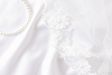 Chic wedding background for design. white satin fabric with soft waves, lace embroidered bridal veil and pearl necklace.
