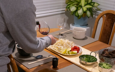 Man pouring red wine and preparing for dinner. Bowl of soup, beef and vegetables on the dinner...