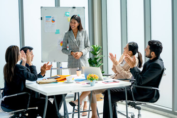 Asian business woman stand in front white board to present the project for co-workers and manager and they look happy to work together in office with day light.