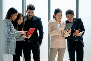 Side view group of Asian business man and woman stand also discuss together near glass windows in office with day light and they look happy and relax during work.