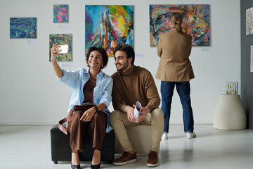 Young couple making selfie portrait on smartphone in gallery of modern art