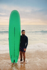 Fototapeta na wymiar Young bearded man with surfboard standing near a beach. Man with surfing board outdoors on a summer day.