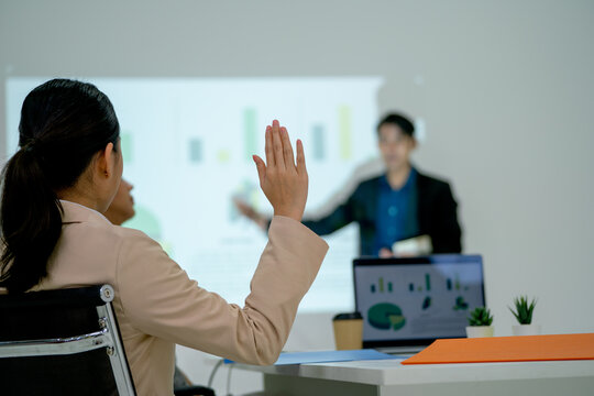 Business woman raise her hand up to ask the question to Asian business man as presentor during the meeting discussion.