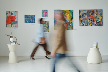 Blurred motion of people visiting art gallery, they walking along the hall among paintings on the...