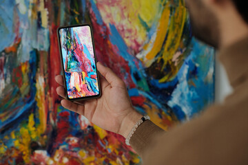 Close-up of man making photo of colorful painting on smartphone in art gallery