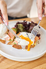Girl cuts avocado toast with salmon and egg . Restaurant dish. Delicious bread with greens and iced coffee