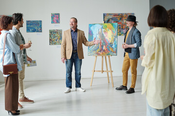 Gallery owner presenting modern art of artist to group of people during exhibition in art gallery