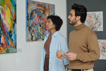 Multiethnic couple watching paintings on the wall while visiting art gallery