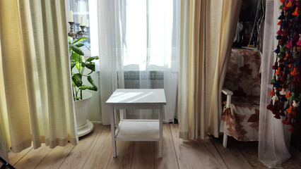 Living room with small table, window, fabric curtains, home flower dieffenbachia. Loft style in the interior. Background and location for photo shoot