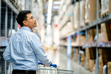 Businessmen enjoy using a trolley cart with looking to the shelves and finding goods in a large...