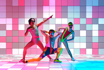 Disco aerobics. Young men in retro, colorful sportswear training against multicolored mosaic studio...