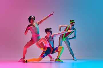 Funny image of three men in stylish, vintage sportswear training aerobics and gymnastics against gradient blue pink studio background. Concept of sportive and active lifestyle, humor, retro style. Ad