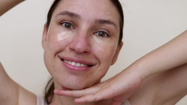 millennial woman doing face procedures,applying under eye patches,vitamin c serum or sheet facial mask.female girl with towel on head having fun,cover mouth with blanket or book.face through palms