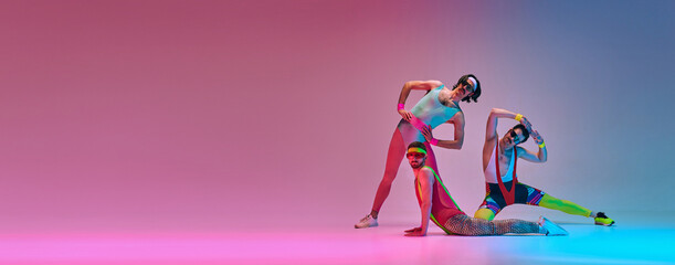 Flexible men in colorful, vintage sportswear stretching against gradient blue pink studio...