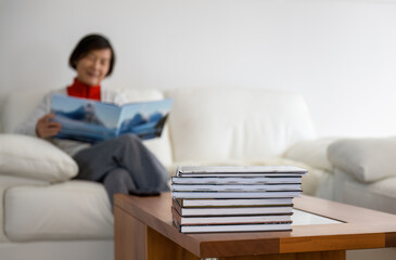 Woman smiling and holding family travel photo album. Selective focus on a pile of photobooks on coffee table.