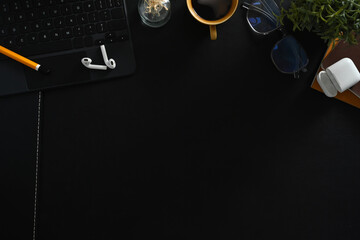 Flat lay notebook, earphones, coffee cup and glasses on dark black surface. Copy space for your text