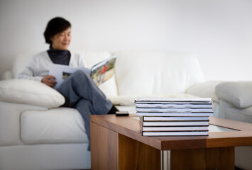 Senior woman smiling and holding family photo album. Selective focus on a pile of photobooks on...