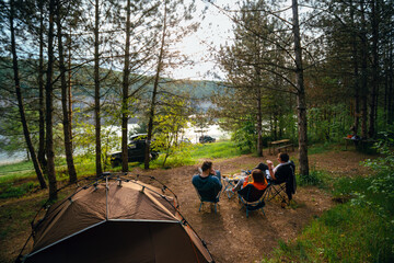 Happy campers. Rearview shot of tThree friends are relaxing with a view of the river. spending time in nature. Quick folding tent equipment, lightweight chairs. Good mood. SUV off road vehicles