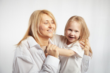 Portrait of a blonde mother and daughter who having communicate and play on a white background. Mom and little girl models pose in the studio. The concept of love, friendship, caring in the family