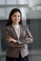 Smiling young beautiful Asian businesswoman looking at camera standing with arms crossed in office