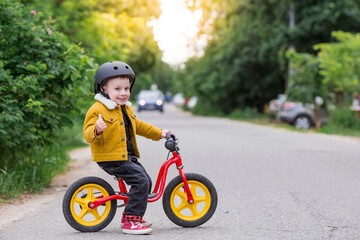 A cheerful little boy rides a running bike in a helmet outdoors. A happy child is engaged in an active sport. Protection. Life insurance and child safety.