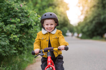 Naklejka premium A cheerful little boy rides a running bike in a helmet outdoors. A happy child is engaged in an active sport. Protection. Life insurance and child safety.