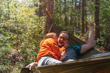 Fototapeta premium Couple man and woman having fun in a hammock, tickling and biting. They laugh and have a good mood, love. Outdoor recreation. Date. Selective focus.