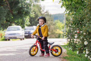 A cheerful little boy rides a running bike in a helmet outdoors. A happy child is engaged in an active sport. Protection. Life insurance and child safety.