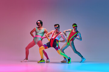 Funny men in vintage, colorful sportswear posing, doing aerobics exercises against gradient blue...