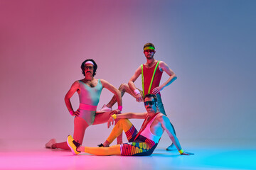 Funny men in vintage, colorful sportswear posing, doing aerobics exercises against gradient blue...