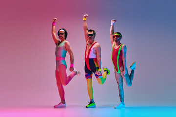 Flexible men in colorful, funny sportswear training, doing stretching exercises on gradient blue pink studio background in neon light. Concept of sportive and active lifestyle, humor, retro style. Ad