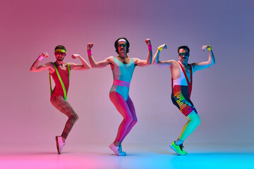 Sport show. Three funny men in colorful sportswear doing aerobics exercises against gradient blue pink studio background in neon light. Concept of sportive and active lifestyle, humor, retro style. Ad - obrazy, fototapety, plakaty