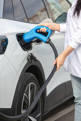 Young business woman refueling her electric car at a EV charging station. Concept of environmentally friendly vehicle. Electric car concept. Green travelling.