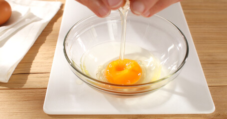 Hands breaking an Egg. Raw egg pours into bowl. Breakfast preparation. Rustic style. Sunny day. Smooth drop. Close up. 