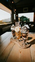 Three glasses of ice cream on a wooden table with a picturesque background.