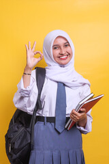 Female Indonesian high school muslim student in white and grey uniform holding books while giving...