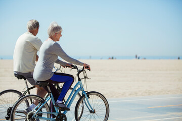 Senior couple riding bicycles on beach - obrazy, fototapety, plakaty