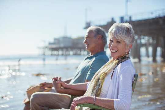 Portrait Of Senior Couple Relaxing In Lawn Chairs On Beach