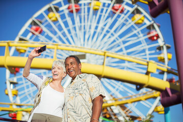 Enthusiastic senior couple taking selfie at amusement park
