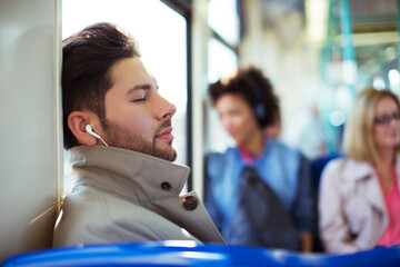 Businessman napping and listening to earbuds on train